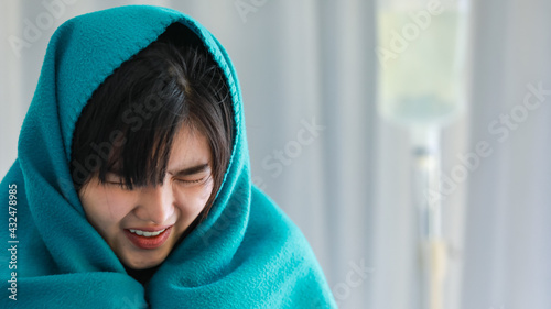 Fotografia Close-up of a severe sick young woman sitting on bed in the hospital, got a flu or cold and covered her body in green blanket to relieve from a frozen fever