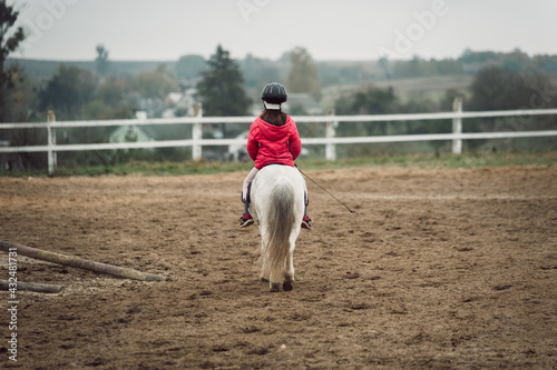 young rider, little girl on a white pony, riding lessons, view from the back