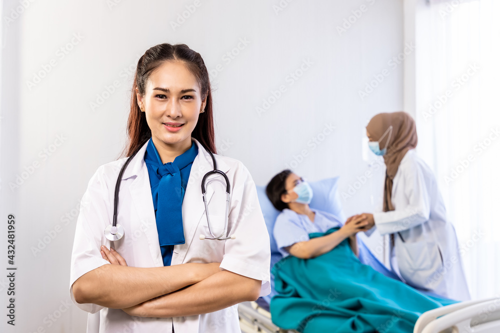 © wirojsid - Portrait of young Asian female doctor in hospital with senior patient in background, cross arms, healthcare or medical service concept.