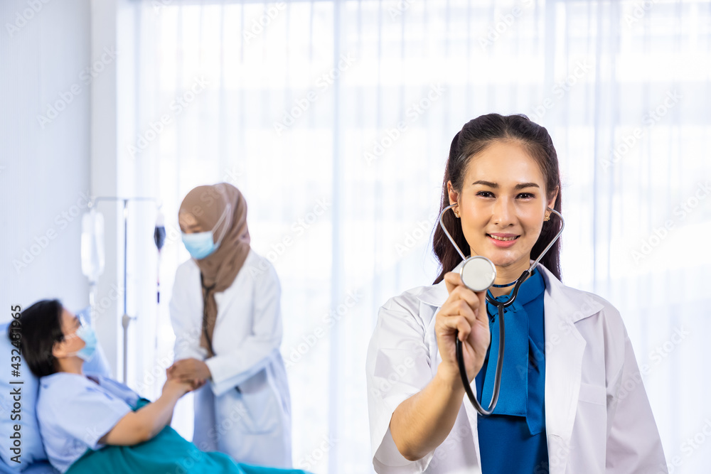 Portrait of young Asian female doctor in hospital with senior patient in background, holding stethoscope, healthcare or medical service concept. Portrait of young Asian female doctor in hospital with senior patient in background, holding stethoscope, healthcare or medical service concept.