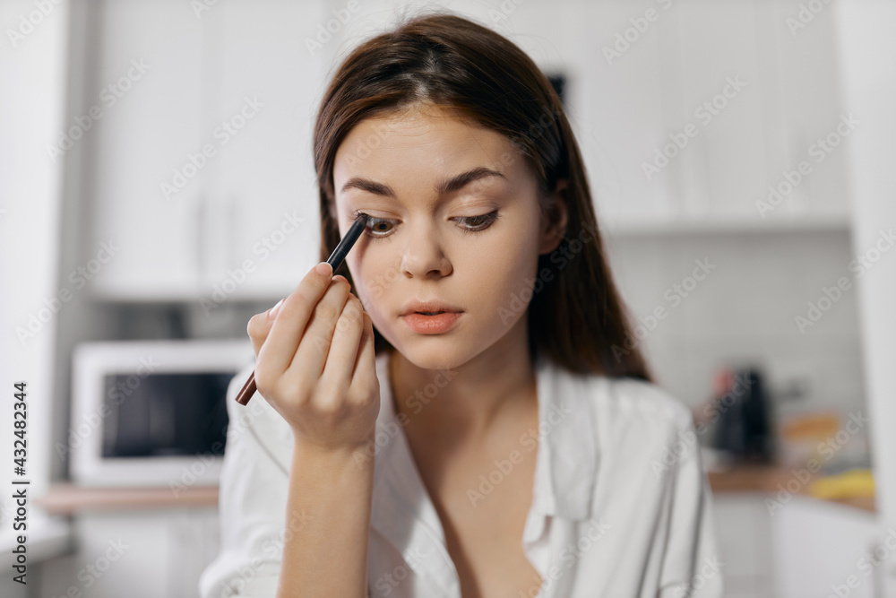 woman makes makeup in the kitchen indoors with eyeliner in hand woman makes makeup in the kitchen indoors with eyeliner in hand