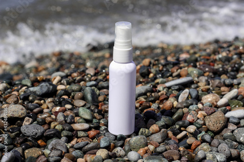  White spay bottle standing at the ocean coast behind the sea. Idea for advertisement and product mock up for example sea salt hair spray, tanning lotion or sunblock lotion
