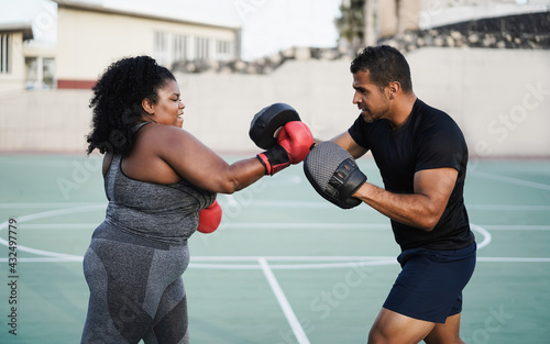 Curvy african girl and personal trainer doing boxing workout session outdoor - Main focus on coach face