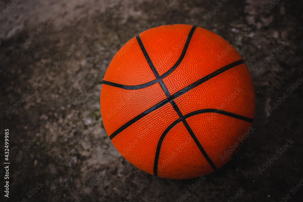 A dirty basketball on a concrete court after a street game. Dark background. A dirty basketball on a concrete court after a street game. Dark background.