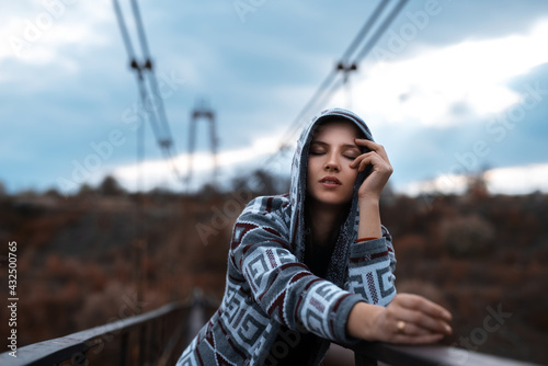 Portrait of young hooded girl standing on abandoned rusty bridge with perspective background. Fashion model posing.
