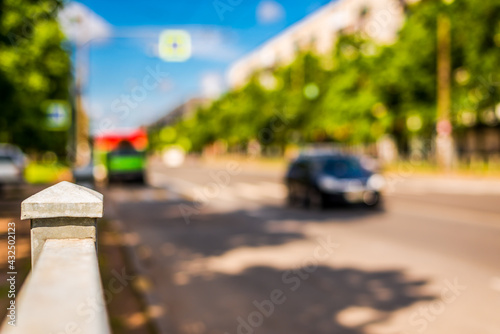 Summer in the city, the car rides down the street with trees. Close up view from the handrail on the sidewalk level