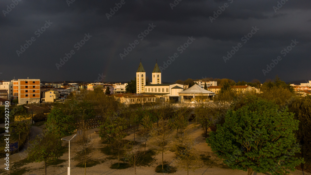 Aerial drone view of Medjugorje at sunset. Catholic Church with rainbow and clouds in background. Međugorje one of the most popular pilgrimage sites for Catholics in Bosnia and Herzegovina.