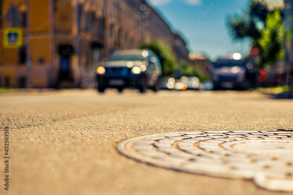 Summer in the city, the car rides down the street with trees. Close up view of a hatch at the level of the asphalt