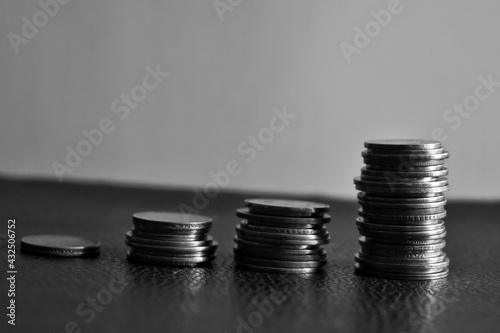 Piled up coins, rupees,dollar in different sizes leaning to the right on white surface and dark background