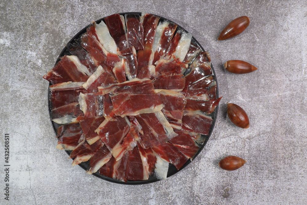 Portion of 100% acorn-fed Iberian ham Dehesa de Extremadura decorated with acorns with dark gray background Portion of 100% acorn-fed Iberian ham Dehesa de Extremadura decorated with acorns with dark gray background
