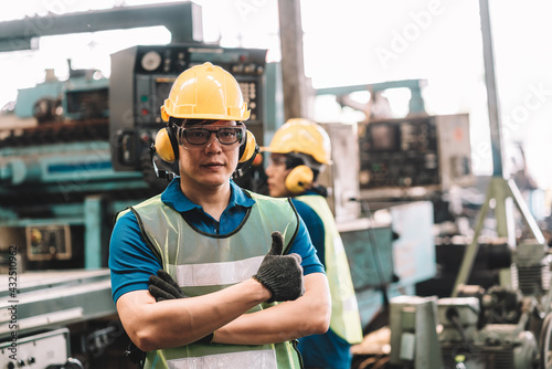 Portrait of Asian worker man working in safety work wear with yellow helmet and glasses l ear muff l glove.male technician asia is happy looking at camera and show thumbs up in factory industrial