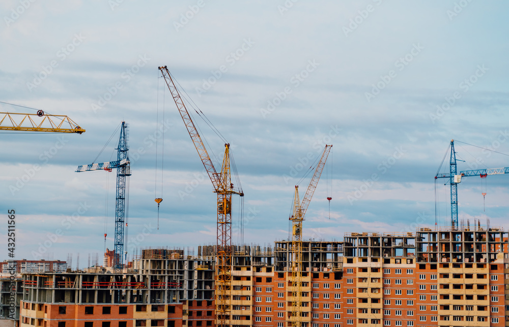Industrial landscape with high construction cranes against the background of a brick house under construction.