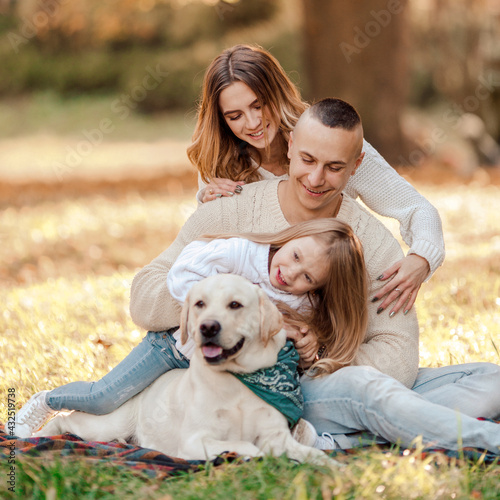 Happy beautiful family with dog labrador is having fun are sitting on green grass in park.