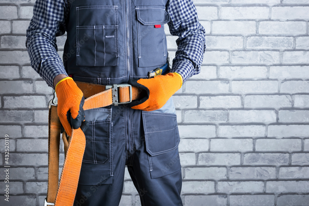 Electrician in uniform puts on a safety belt. Personal Protective Equipment very importance for health protection. Safety at work concept. Electrician in uniform puts on a safety belt. Personal Protective Equipment very importance for health protection. Safety at work concept.