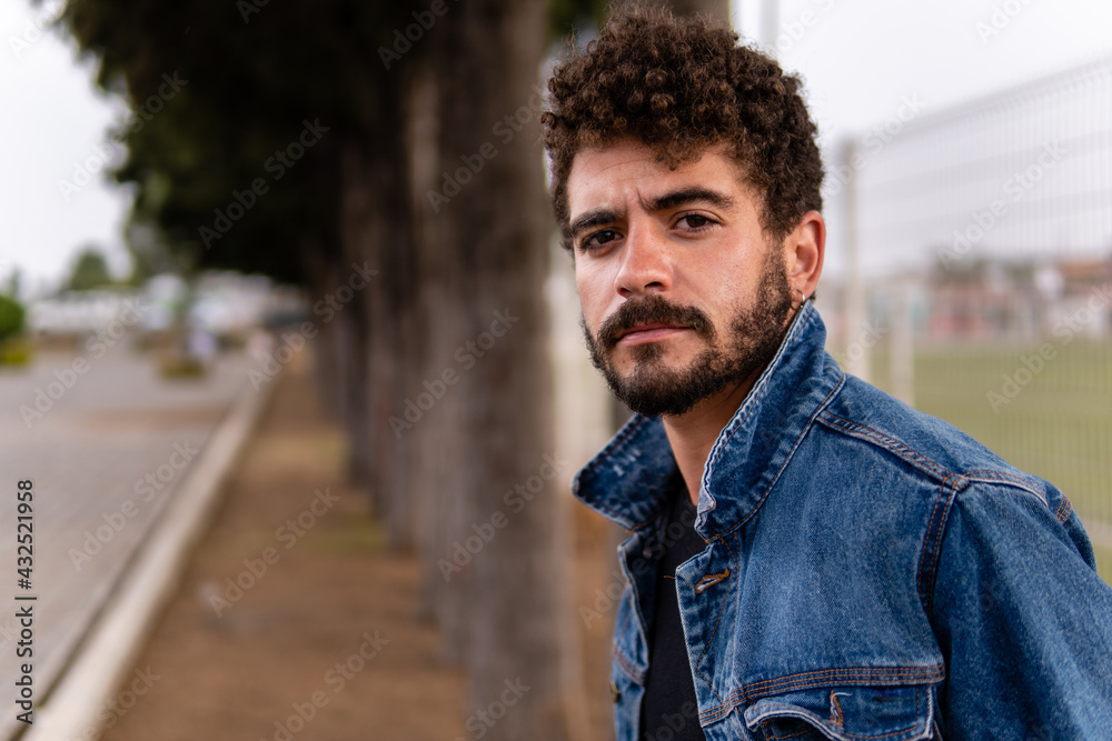 Handsome young man with curly hair and beard wearing denim posing in a ...