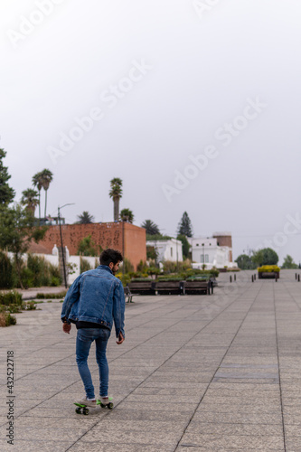 Handsome young man with curly hair and a beard wearing denim skateboarding in an empty public park during a rainy day