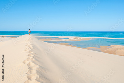 Young man walking through the sand of a dune towards the turquoise and heavenly beach of an island