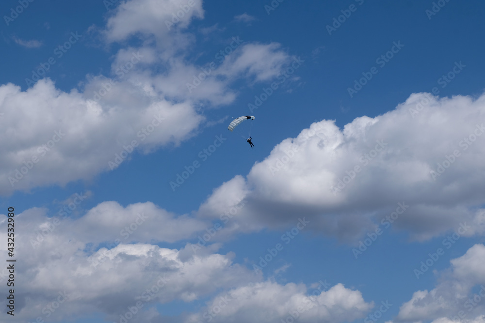 Skydiving. A skydiver is in the cloudy blue sky.