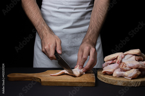 Raw chicken wings on a black background. The chef prepares chicken wings on a dark background. Fresh chicken meat.