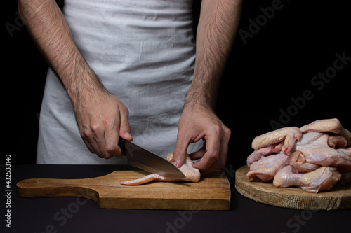 Raw chicken wings on a black background. The chef prepares chicken wings on a dark background. Fresh chicken meat.