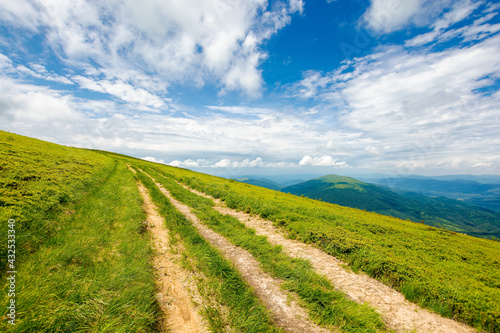 country dirt road through grassy hillside. mountain ridge in the distance beneath a gorgeous cloudscape on the blue sky. travel backcountry concept