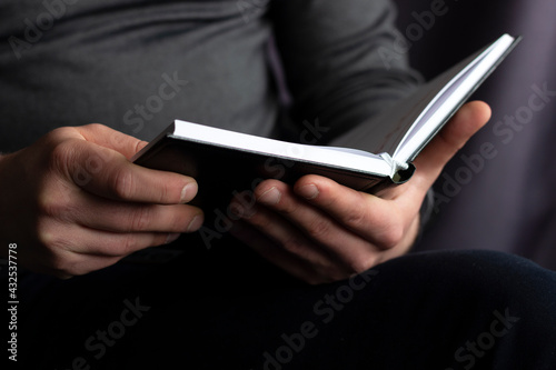 Close up view of male hands holding a book. Young man relaxes at home reading a book. Selective focus on hand, blurred background.