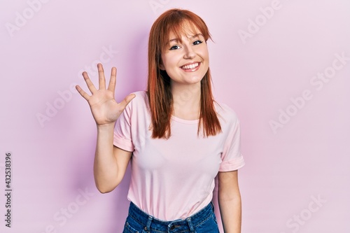 Redhead young woman wearing casual pink t shirt showing and pointing up with fingers number five while smiling confident and happy.