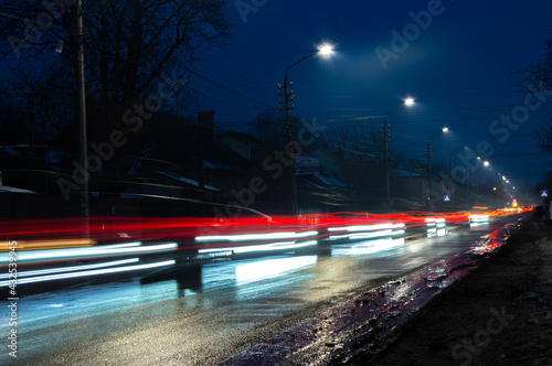 night dark photo of blur of intermittent red-blue light from car headlights, along the road with lantern light