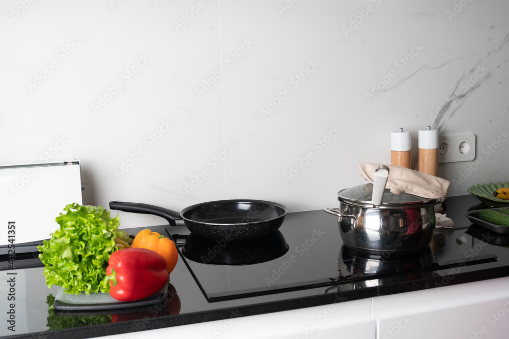 pot and frying pan stands on stove, green salad and pepper lying near it. Preparing meal pot and frying pan stands on stove, green salad and pepper lying near it. Preparing meal