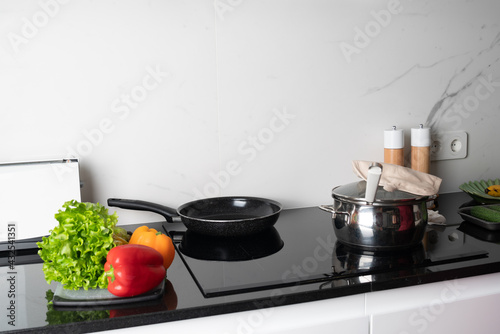 pot and frying pan stands on stove, green salad and pepper lying near it. Preparing meal