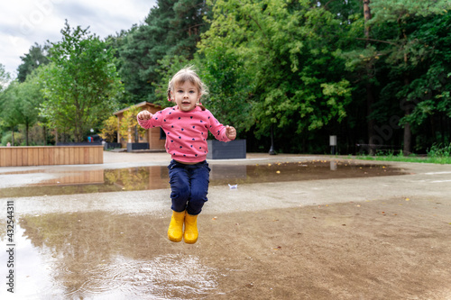 happy child girl running and jumping in puddles after rain in summer, jump in the air © Елена Гурова