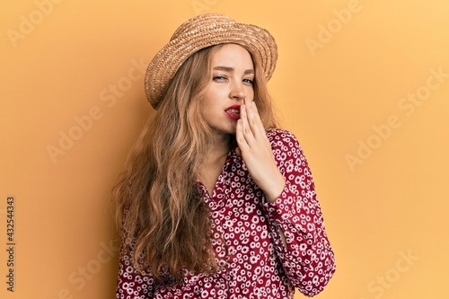 Beautiful blonde caucasian woman wearing summer hat bored yawning tired covering mouth with hand. restless and sleepiness.