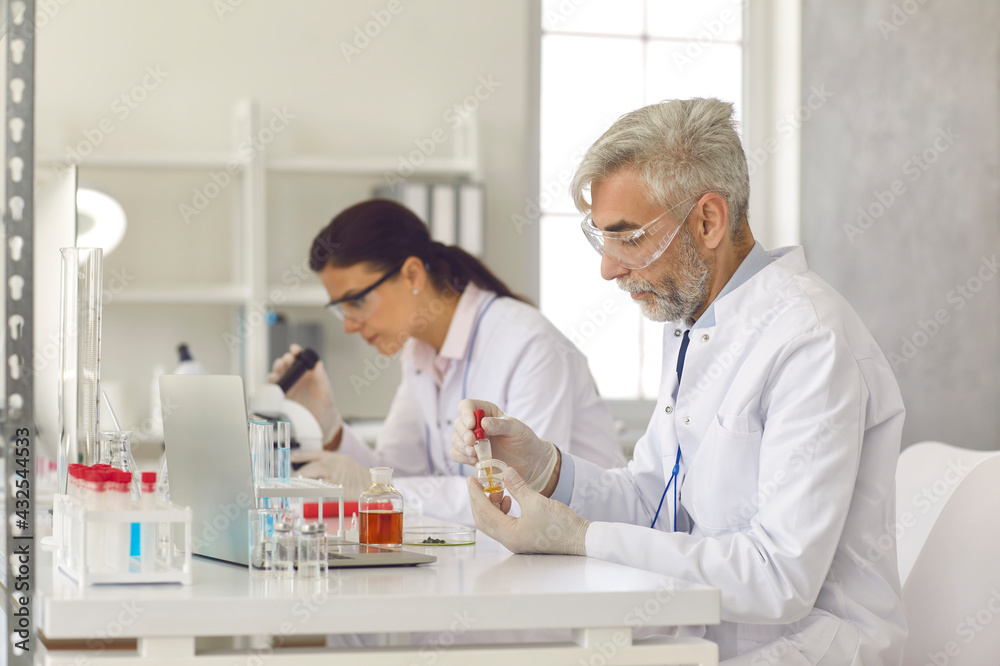 Old and young scientist working at science laboratory conducting experiment doing analysis learning bacteria with microscope and examining chemical test sample in tube. Science research and education Old and young scientist working at science laboratory conducting experiment doing analysis learning bacteria with microscope and examining chemical test sample in tube. Science research and education