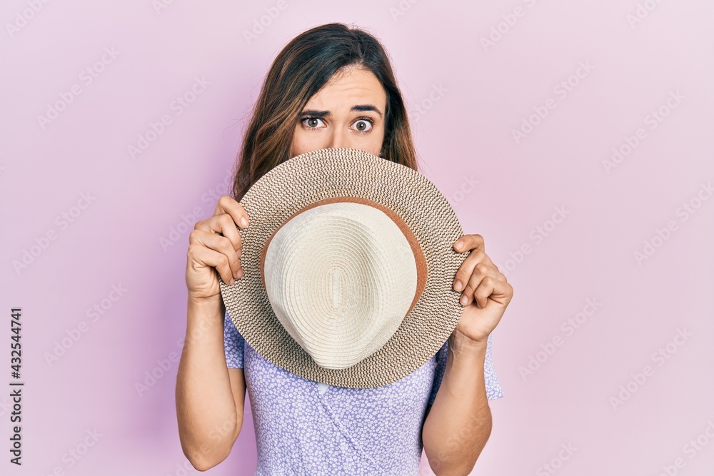 Young hispanic girl wearing summer hat covering mouth clueless and confused expression. doubt concept. Young hispanic girl wearing summer hat covering mouth clueless and confused expression. doubt concept.