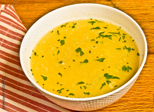 top view, close distance of a white bowl of egg drop soup with chopped parsley on wood cutting board