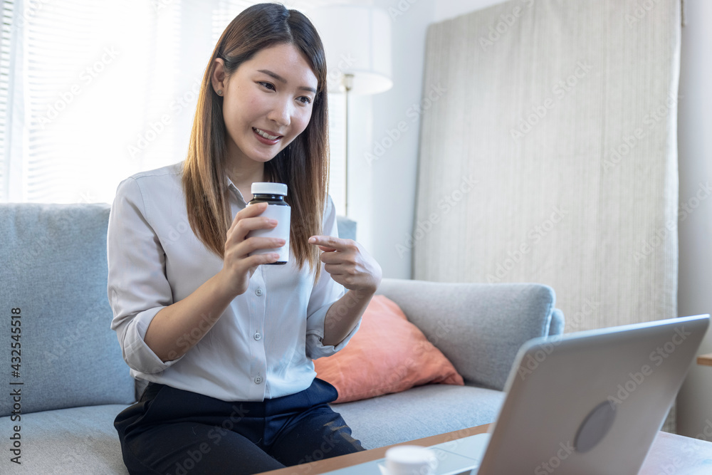 Asian woman sitting on the sofa while making video call over laptop with her doctor. Asian woman sitting on the sofa while making video call over laptop with her doctor.