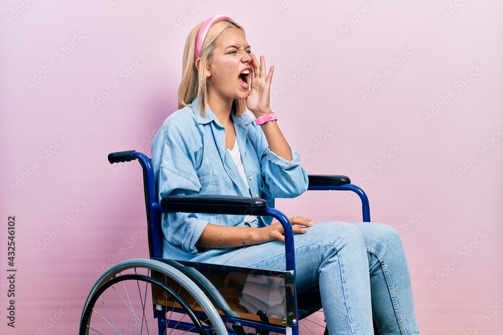 Beautiful blonde woman sitting on wheelchair shouting and screaming loud to side with hand on mouth. communication concept. Beautiful blonde woman sitting on wheelchair shouting and screaming loud to side with hand on mouth. communication concept.