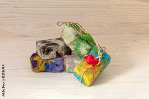 Natural handmade soap in colored wool with red heart on light natural wooden background. The concept of a washcloth peeling. Self-care, commitment to eco-friendly products.