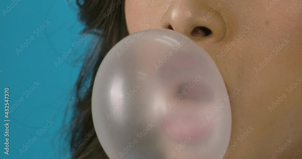 Portrait and big close up shot of young beautiful asian woman blowing gum in blue background. Fashion, travel and beauty concept.