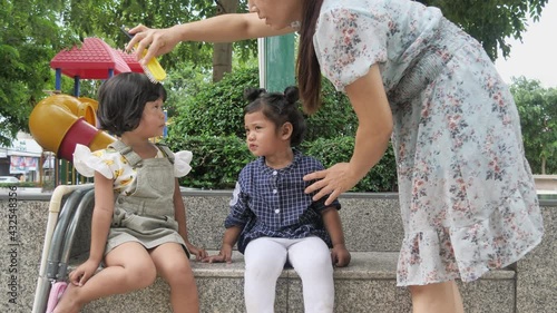 Mom combing the two lovely daughters' hair at the playground.