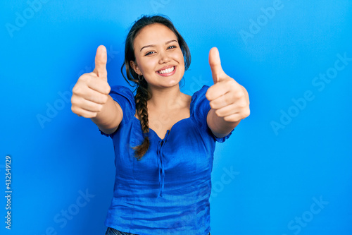 Young hispanic girl wearing casual clothes approving doing positive gesture with hand, thumbs up smiling and happy for success. winner gesture. © Krakenimages.com