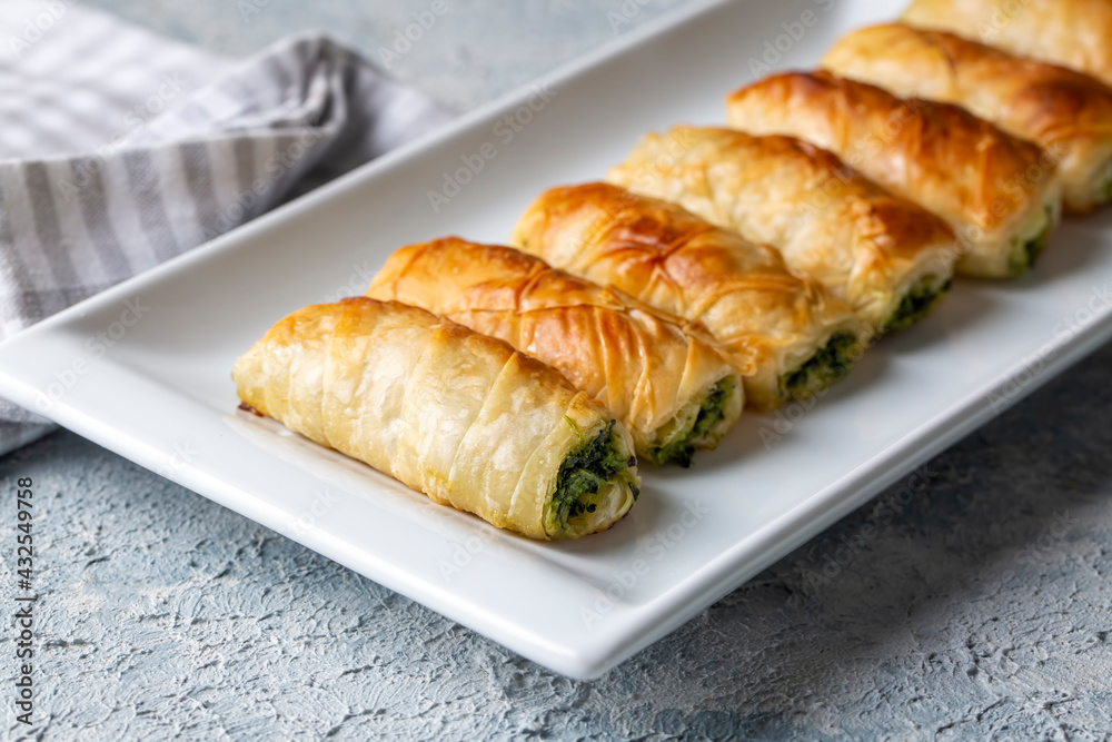 Turkish borek rolls with spinach and cheese on the white plate. A traditional Turkish pastry, Turkish name; rulo borek or sigara boregi. Turkish borek rolls with spinach and cheese on the white plate. A traditional Turkish pastry, Turkish name; rulo borek or sigara boregi.