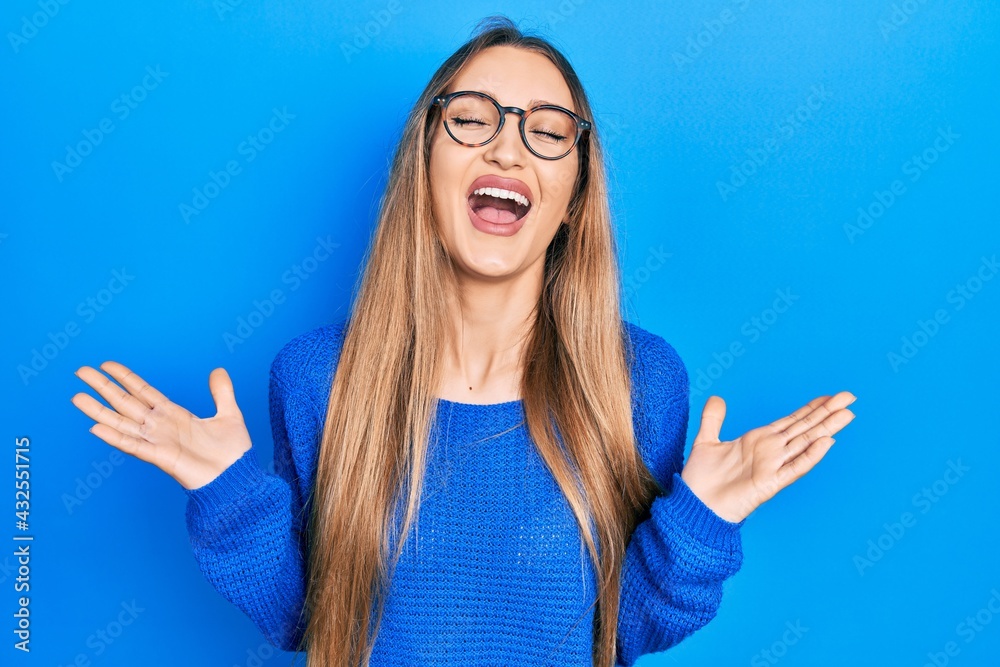 Young blonde girl wearing casual clothes and glasses celebrating mad and crazy for success with arms raised and closed eyes screaming excited. winner concept Young blonde girl wearing casual clothes and glasses celebrating mad and crazy for success with arms raised and closed eyes screaming excited. winner concept