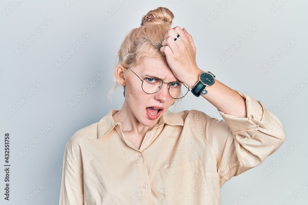 Beautiful caucasian woman with blond hair wearing casual look and glasses surprised with hand on head for mistake, remember error. forgot, bad memory concept.