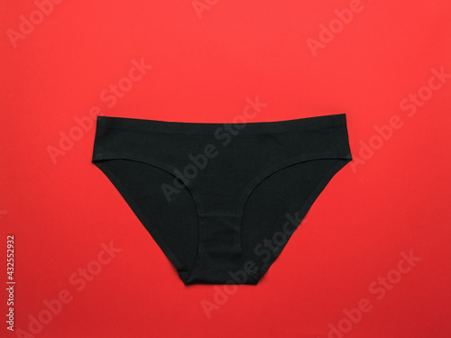 Classic women's black panties on a bright red background. Flat lay. photo