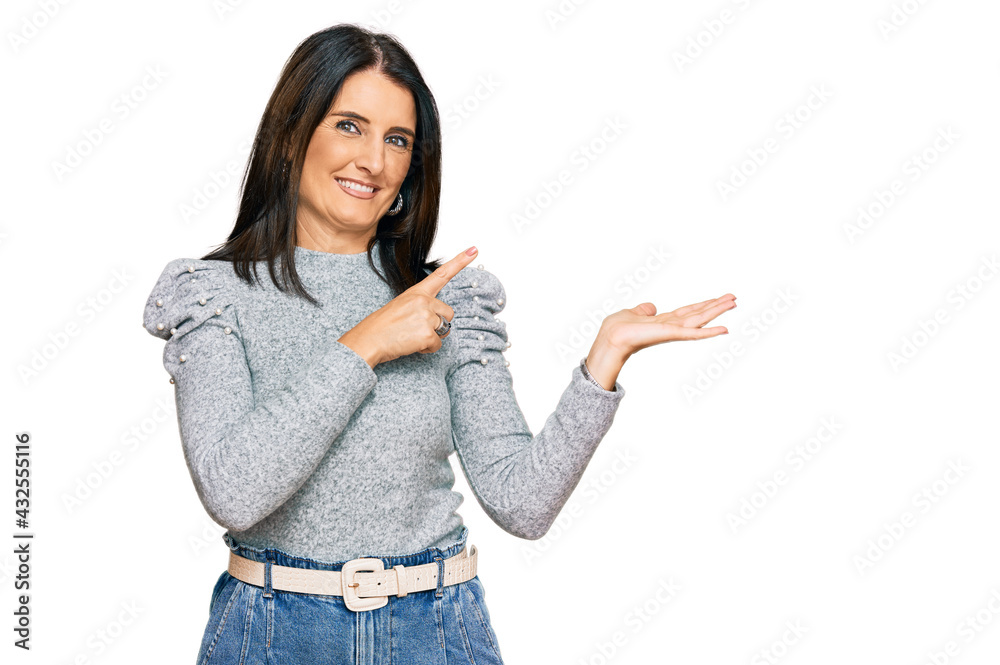 Middle age brunette woman wearing casual clothes amazed and smiling to the camera while presenting with hand and pointing with finger.