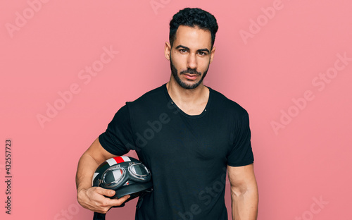 Fotografie Hispanic man with beard holding motorcycle helmet thinking attitude and sober ex
