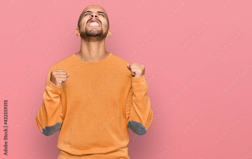 Hispanic adult man wearing casual winter sweater very happy and excited doing winner gesture with arms raised, smiling and screaming for success. celebration concept. Hispanic adult man wearing casual winter sweater very happy and excited doing winner gesture with arms raised, smiling and screaming for success. celebration concept.