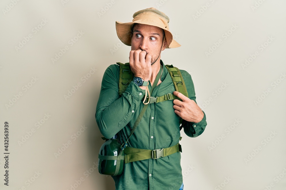 Handsome man with beard wearing explorer hat and backpack looking stressed and nervous with hands on mouth biting nails. anxiety problem. Handsome man with beard wearing explorer hat and backpack looking stressed and nervous with hands on mouth biting nails. anxiety problem.