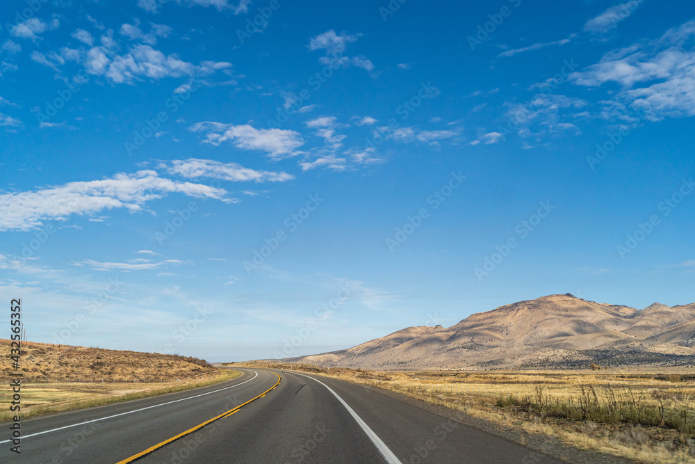 Two lane road in the arid Sierra Nevada's leading to mountains against blue sky